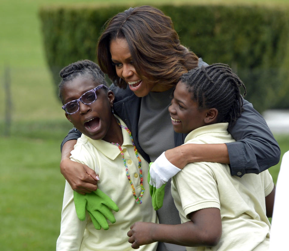 First lady Michelle Obama hugs two students as she arrives to plant the White House Kitchen Garden at the White House in Washington, Wednesday, April 2, 2014. (AP Photo/Susan Walsh)