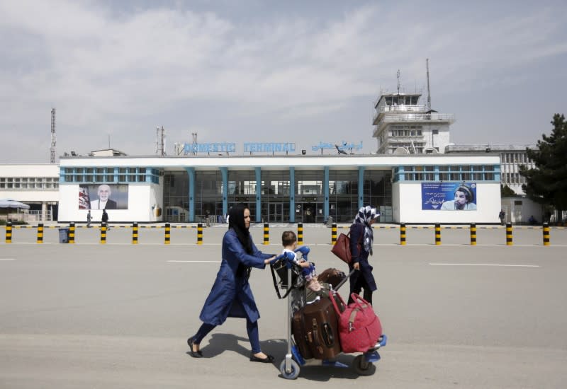 FILE PHOTO: Afghan passengers walk in front of Hamid Karzai International Airport in Kabul