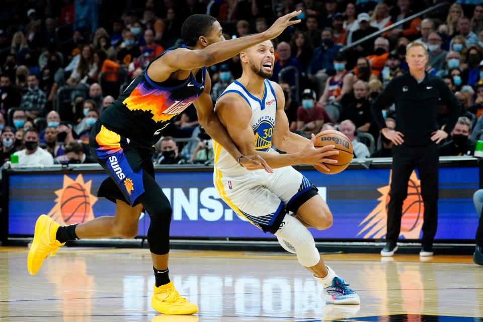 Golden State Warriors guard Stephen Curry (30) drives as Phoenix Suns forward Mikal Bridges defends during the first half of an NBA basketball game, Tuesday, Nov. 30, 2021, in Phoenix. (AP Photo/Matt York).
