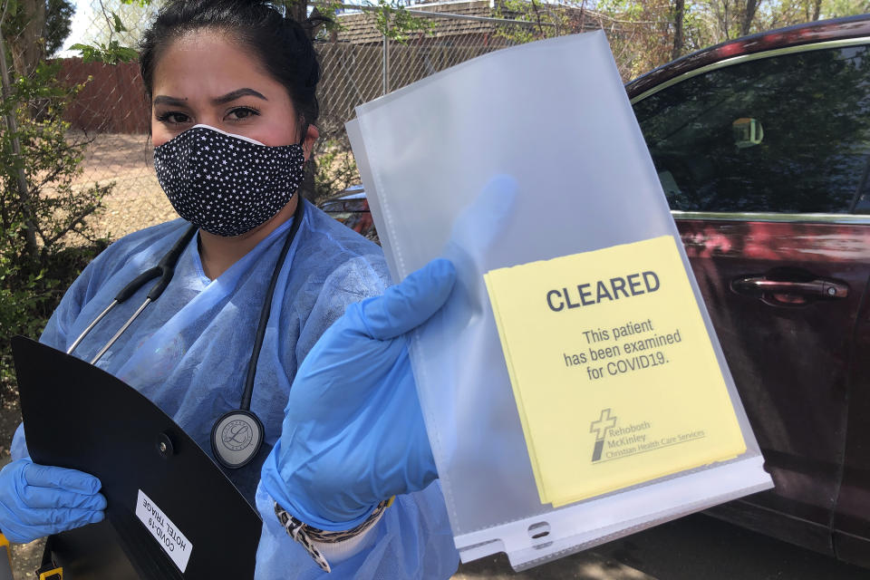 Certified Medical Assistant Shaniya Wood displays a certification card that homeless residents can use to show they are free of the coronavirus to gain access to shelters and other services, Thursday, May 7, 2020 in Gallup, N.M. More than 100 homeless people in Gallup are being housed temporarily in motel rooms and tested for the coronavirus to contain an outbreak that raced through a detox center in early April. Gallup was under a lockdown order with police roadblocks from New Mexico Gov. Michelle Lujan Grisham in efforts to stem the rapid transmission of COVID-19 in the area. Gallup and surrounding McKinley County are one of the worst rural hot spots for the coronavirus infections in the U.S. (AP Photo/Morgan Lee)