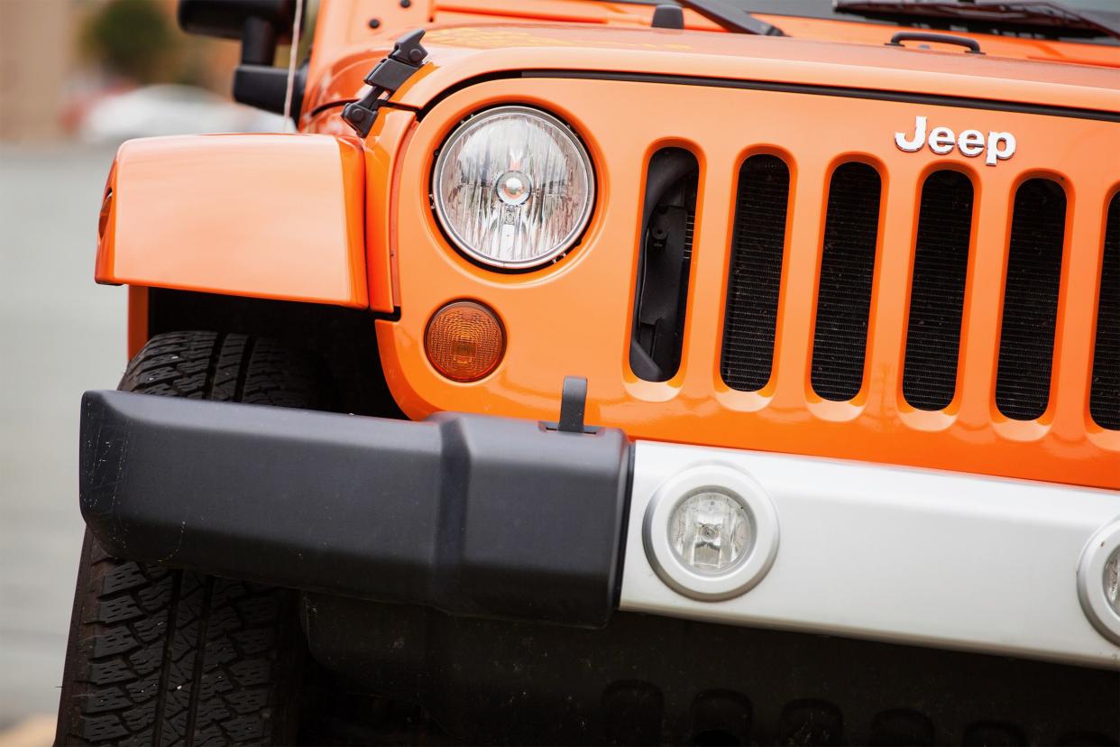 Close up of orange Jeep Wrangler front with blurred background.