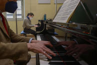 Viola Arena, background, wears a sanitary face mask as she plays the piano piano behind a transparent panel to curb the spread of COVID-19, during a lesson with maestro Andrea Carcano at the Giuseppe Verdi Music Conservatory, in Milan, Italy, Thursday, April 29, 2021. Whatever the instrument, flute, violin or drums, students at Italy's oldest and largest music conservatory have been playing behind plexiglass screens during much of the pandemic as the Conservatory found ways to preserve instruction throughout Italy’s many rolling lockdowns. (AP Photo/Antonio Calanni)