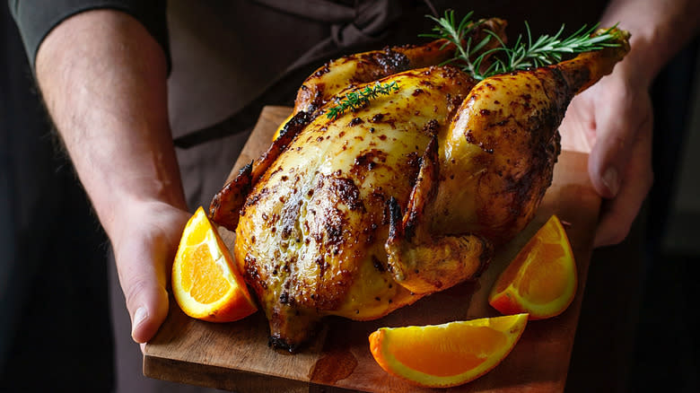 Hands holding roast chicken with oranges