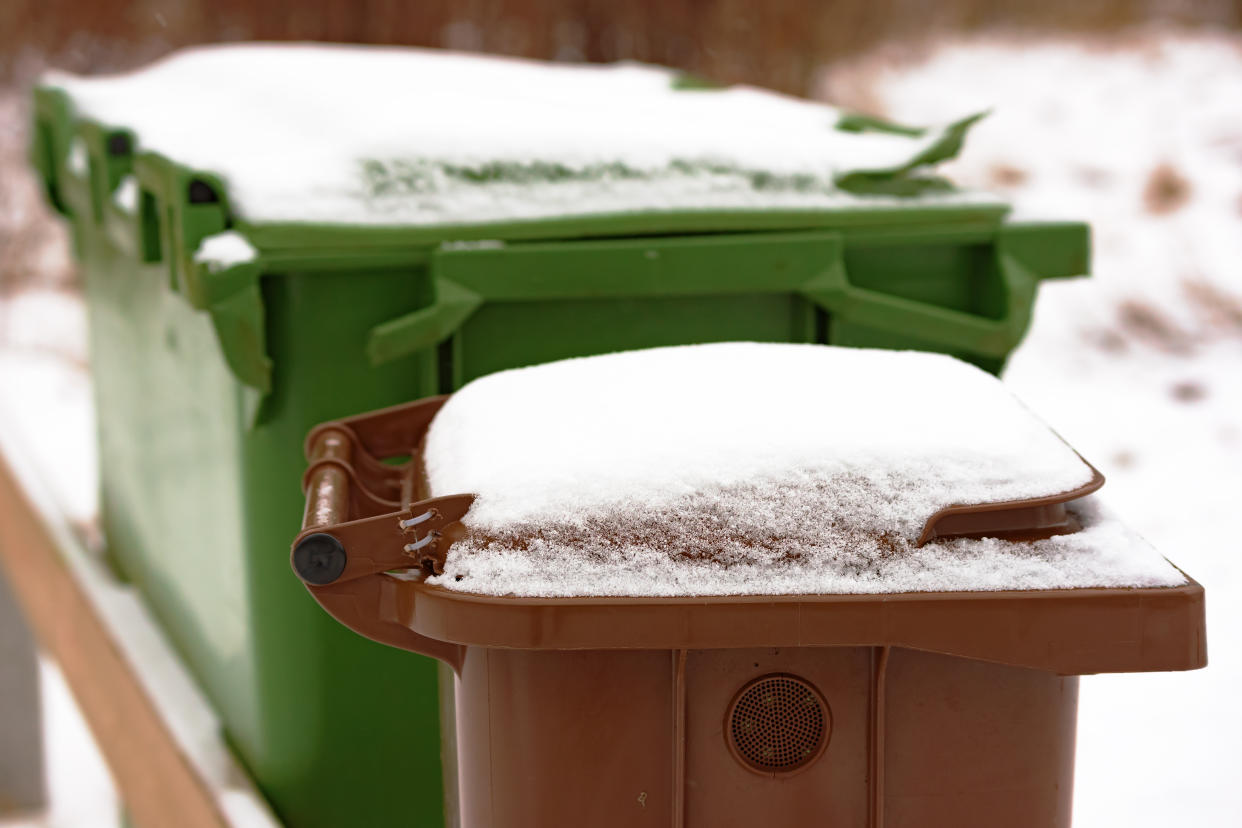 Snow covered brown trash bin lid in winter. Bin has air vent at side.