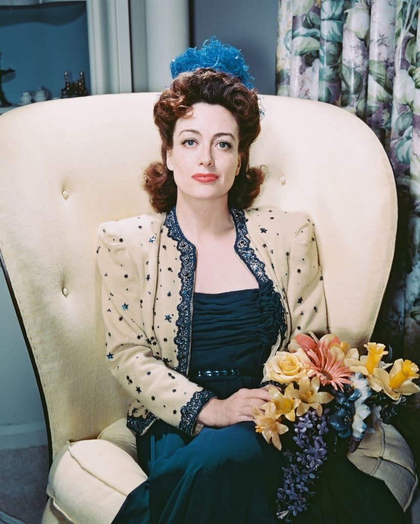 A vintage-style portrait of Joan seated with flowers, in an embellished dress with a headpiece