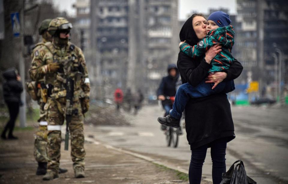 A woman holds and kisses a child next to Russian soldiers in a street of Mariupol on 12 April 2022 (AFP via Getty)