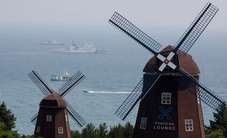 FILE PHOTO: Dutch-style windmills at a hotel provide the foreground as Korea Coast Guard ships patrol along the coast of Seogwipo on Jeju Island May 30, 2009. REUTERS/Lee Jae-Won/File Photo