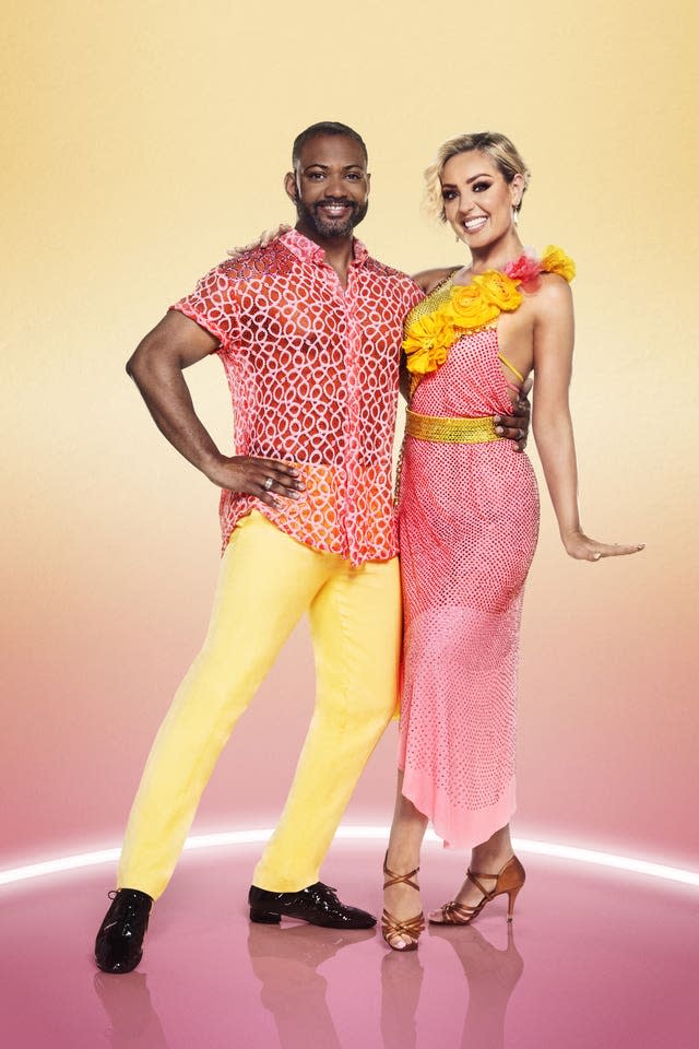 A man wearing a pink top and yellow trousers, and a woman in a pink dress