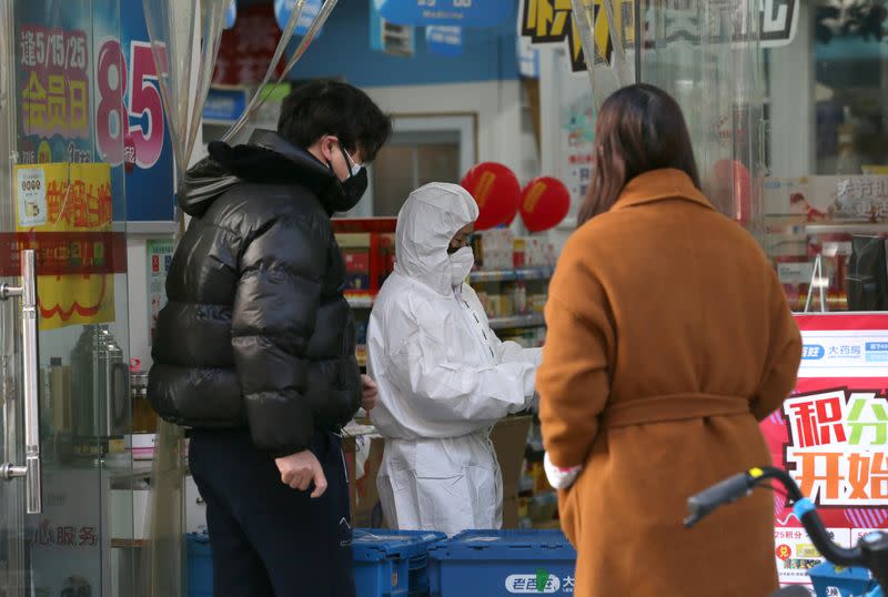 Worker in protective suit serves customers at a pharmacy following an outbreak of the new coronavirus in Wuhan