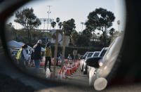 Health care workers are reflected in the rear view mirror of a vehicle as they prepare to distribute a COVID-19 vaccine to Los Angeles residents as they wait in line in their cars in the early morning at Dodger Stadium on Tuesday, Jan. 26, 2021, in Los Angeles. California is revamping its vaccine delivery system to give the state more control over who gets the shots following intense criticism of a slow and scattered rollout by counties. (AP Photo/Richard Vogel)