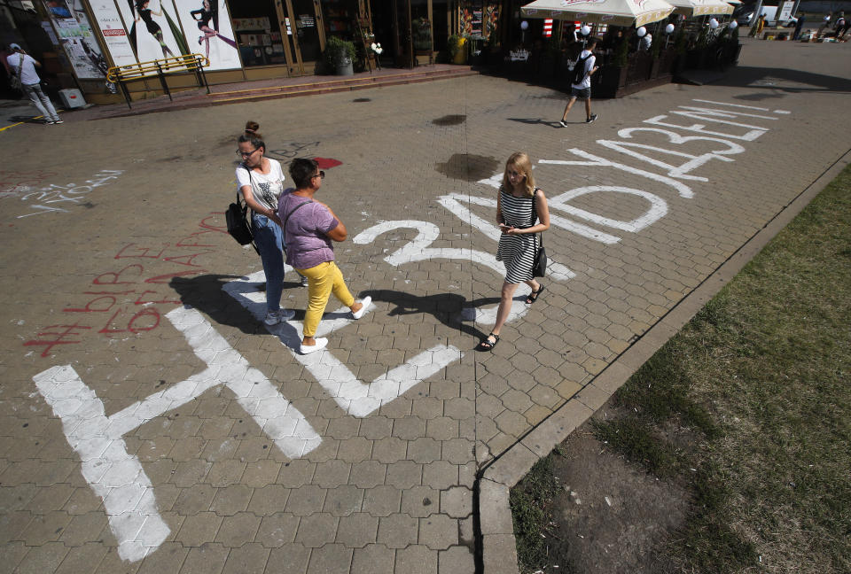 FILE - In this Monday, Aug. 24, 2020 file photo, People walk along the sign "We will not forget!" painted on the sidewalk near the place where Alexander Taraikovsky died amid the clashes protesting the election results, in Minsk, Belarus. Belarusian authorities long ago removed the makeshift memorial to Alexander Taraikovsky, who was shot by police at the start of last year's massive protests against the country's autocratic president, and in December two people were handed two-year prison sentences for writing "We will not forget!" on the pavement where Taraikovsky was killed. (AP Photo/Dmitri Lovetsky, File)