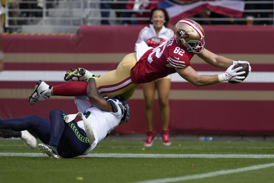 El tight end de los 49ers de San Francisco, Ross Dwelley (82), se lanza para anotar pese a la marca del safety Quandre Diggs en la primera mitad del partido de la NFL en Santa Clara, California, el domingo 18 de septiembre de 2022. (AP Foto/Tony Avelar)