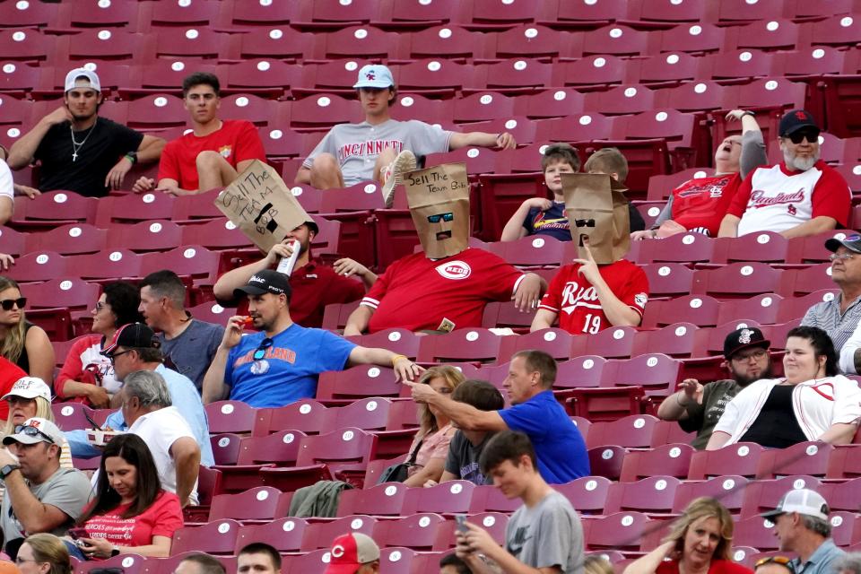 Reds fans wear paper bags on their heads, two of which read, 'Sell the team, Bob,' referencing a call for Cincinnati Reds CEO Bob Castellini to sell the team.