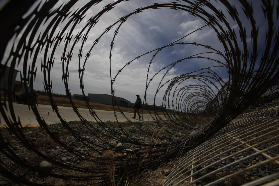 A journalist walks past a fallen section of fencing during a media tour of the now closed Laguna del Toro maximum security facility on the former Islas Marias penal colony located off Mexico's Pacific coast, Saturday, March 16, 2019. All that remains for now are a few goats, some cattle and once-domesticated cats that roam the main island where thousands of prisoners once lived. (AP Photo/Rebecca Blackwell)