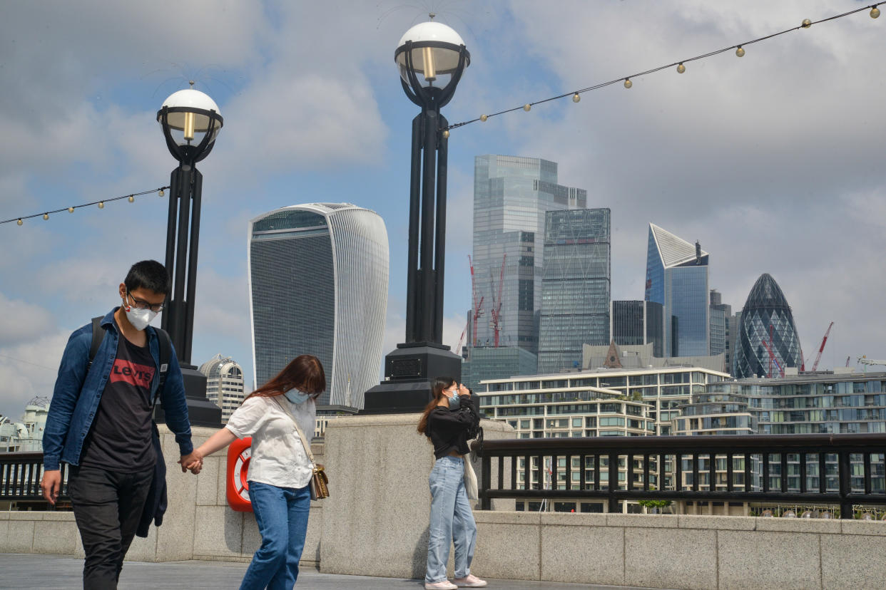 People walk next to the Thames with London's financial district in the background