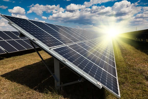 Solar farm in a grassy field with the sun in the background.