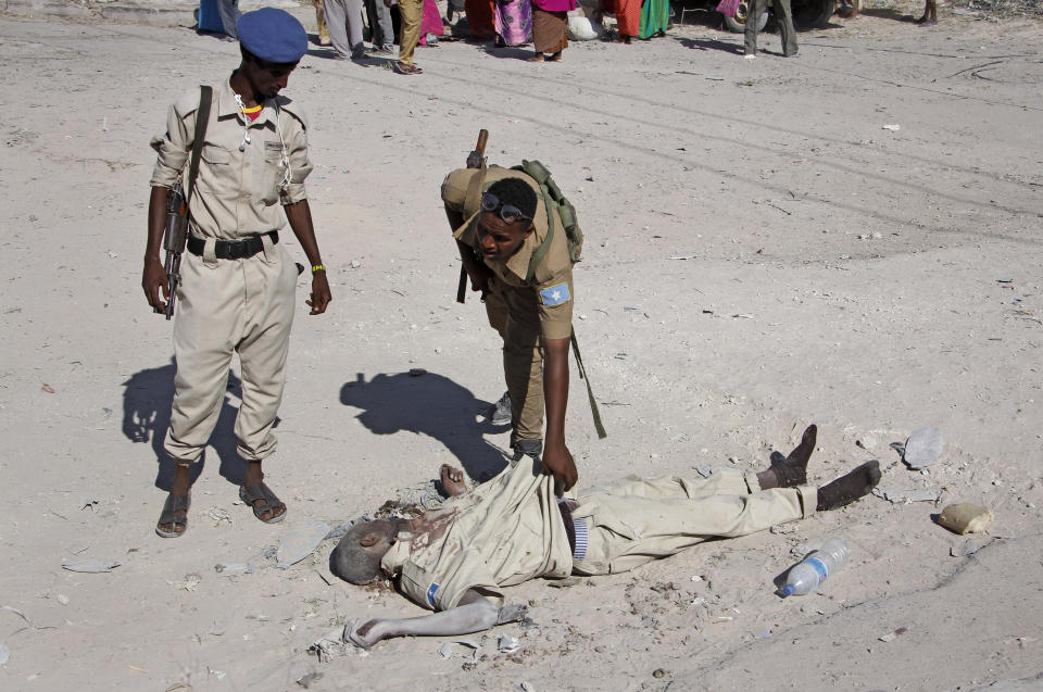 Somali government soldiers check the dead body of a suspected attacker after a suicide car bomb attack on a government building in the capital Mogadishu, Somalia, Saturday, March 23, 2019. Al-Shabab gunmen stormed the government building after a suicide car bombing, killing at least five people including the country's deputy labor minister, police said, in the latest attack by Islamic extremist fighters in the Horn of Africa nation. (AP Photo/Farah Abdi Warsameh)