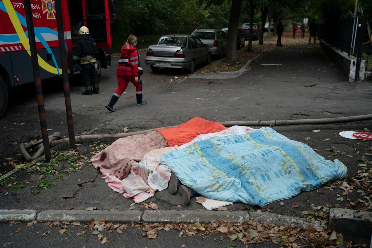 A member of the rescue service walks past three bodies, covered by blankets, following a Russian attack in Dnipro, Ukraine, Monday, Oct. 10, 2022. Explosions on Monday rocked multiple cities across Ukraine, including missile strikes on the capital Kyiv for the first time in months. 