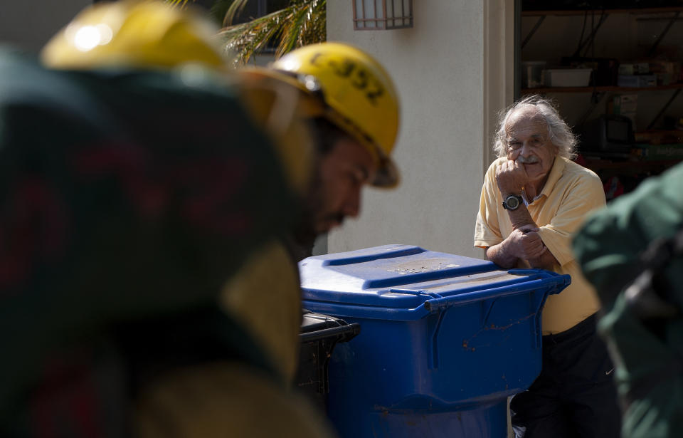 A man watches as firefighters prepare to enter his backyard to fight a wildfire in the Pacific Palisades area of Los Angeles, Monday, Oct. 21, 2019. The blaze broke out Monday morning in a coastal canyon of the affluent Pacific Palisades neighborhood. The flames quickly churned uphill through dry brush as helicopters made water drops to keep it from reaching large houses at the top of a bluff. Firefighters in backyards are using water hoses to protect structures. The cause is unknown. (AP Photo/Christian Monterrosa)