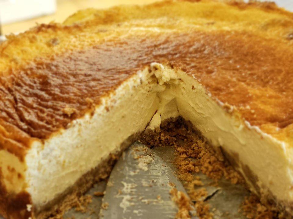 A partially eaten slice of creamy, baked cheesecake with a crumbly crust, showcasing its smooth texture and rich layers