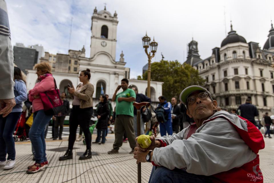 Un hombre come una pera mientras la gente hace fila para recibir fruta gratis frente a la casa de gobierno en Buenos Aires, Argentina, el martes 23 de abril de 2019. (AP Foto / Tomás F. Cuesta)