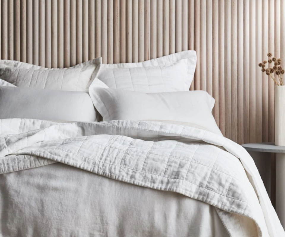 A cream quilted double bed in front of pale wooden slats.