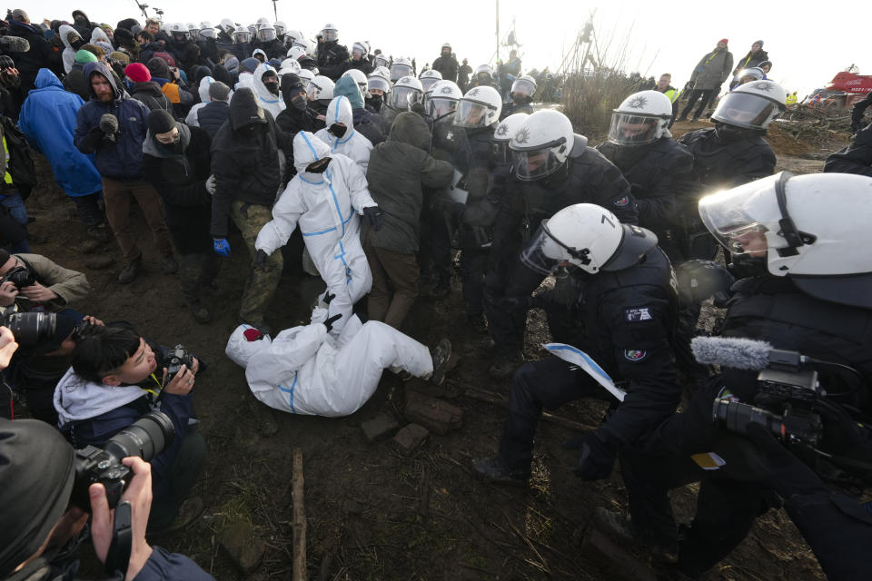 Police officers scuffle with demonstrators at the village of Luetzerath near Erkelenz, Germany, Tuesday, Jan. 10, 2023. The village of Luetzerath is occupied by climate activists fighting against the demolishing of the village to expand the Garzweiler lignite coal mine near the Dutch border. Poster read: „1,5 degrees celsius means: Luetzerath stays". (AP Photo/Michael Probst)