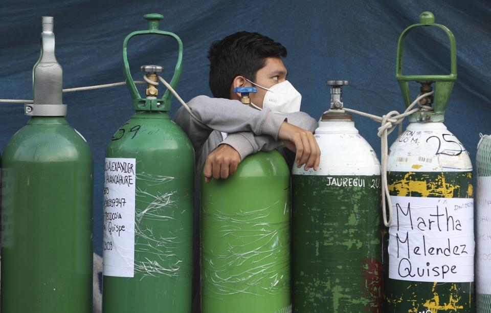 A youth rests on his empty oxygen cylinder waiting for a refill shop to open in the San Juan de Lurigancho neighborhood of Lima, Peru, Monday, Feb. 22, 2021. A crisis over the supply of medical oxygen for coronavirus patients has struck in Africa and Latin America, where warnings went unheeded at the start of the pandemic and doctors say the shortage has led to unnecessary deaths. (AP Photo/Martin Mejia)