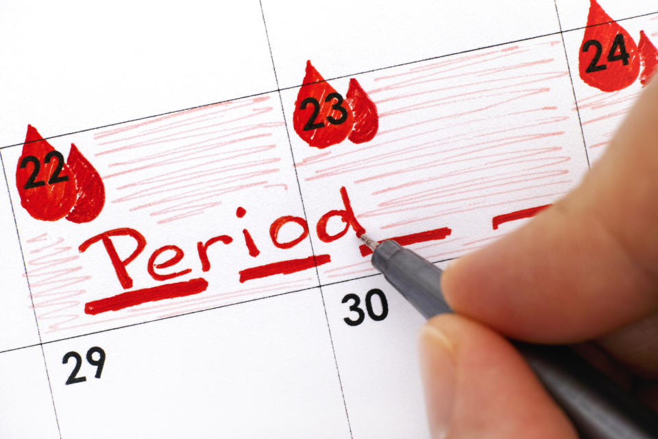 Woman fingers with pen writing reminder Period in calendar. Close-up.