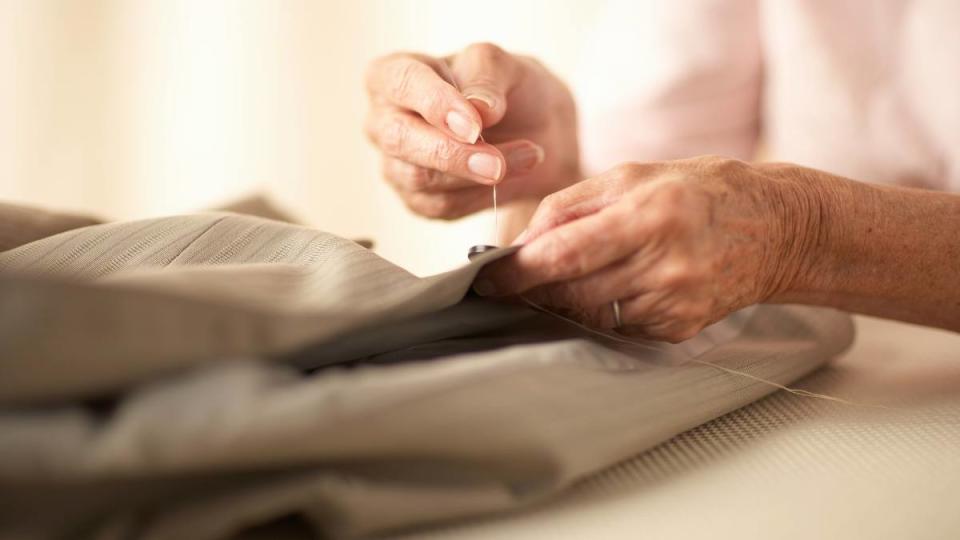 Uses For Dental Floss: Senior woman sewing button on jacket, close-up of hands