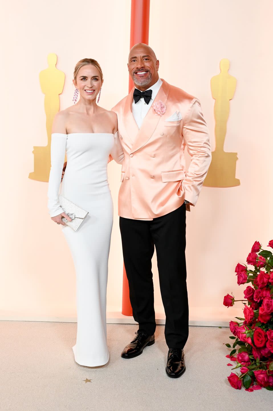 Emily Blunt in a long white strapless dress and Dwayne Johnson in a black bow tie, trousers and a peach satin tuxedo