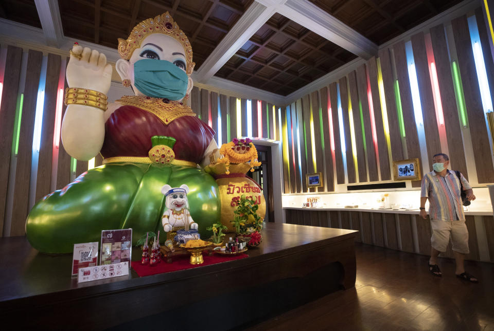 A visitor looks at a giant statue of Nagkwank wearing a face mask at the Siam Musuem in Bangkok, Thailand, Friday, May 29, 2020. Nagkwank is a benevolent spirit who is deemed to bring luck and prosperity. She is the patron deity of all merchants and salesmen and can be seen in very many business establishments in Thailand. Thai authorities allowed museum and other businesses to reopen, selectively easing restrictions against the coronavirus. (AP Photo/Sakchai Lalit)