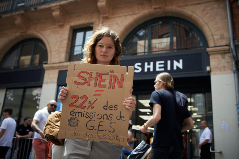 An Extinction Rebellion protestor holds a placard reading "SHEIN = 22% of warming gas emitted for youths" in front of a pop-up store.<span class="copyright">Alain Pitton—NurPhoto/Getty Images</span>