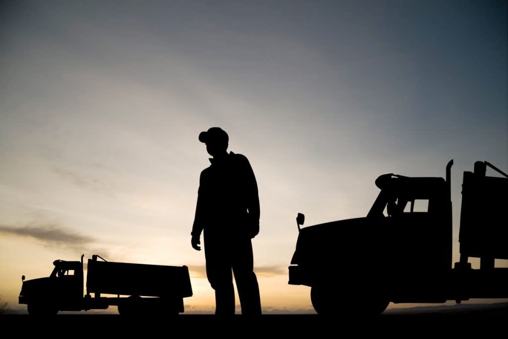 A man stands in-between two trucks as the sun sets. 