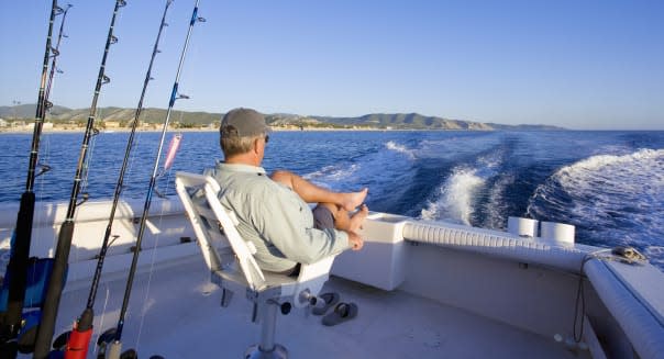 Man sitting in back of sport fishing boat, rear view