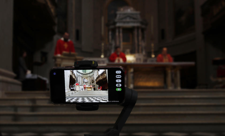 A smartphone films priests praying during the Passion of Christ Mass on Good Friday inside the Santissima Redentore church in Seriate, near Bergamo, one of the areas worst hit by coronavirus, Northern Italy, Friday, April 10, 2020. For most people, the new coronavirus causes only mild or moderate symptoms. The new coronavirus causes mild or moderate symptoms for most people, but for some, especially older adults and people with existing health problems, it can cause more severe illness or death. (AP Photo/Antonio Calanni)