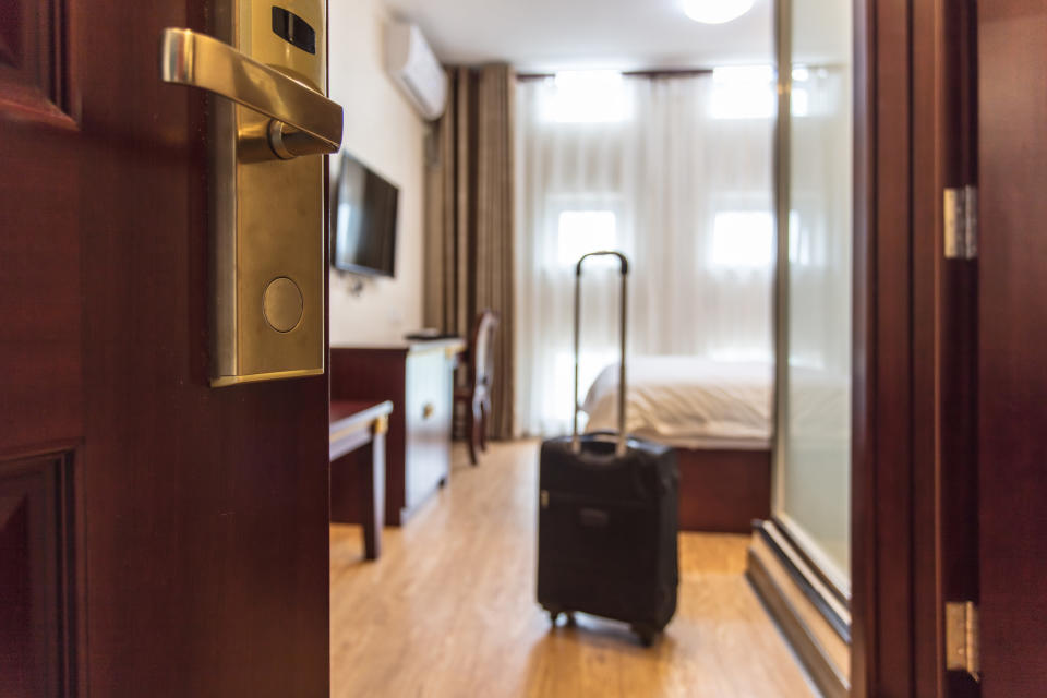 Door opening to a hotel room with a carry-on luggage in the center of the room