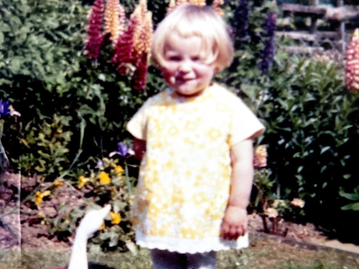 A vintage photo of a little girl in a yellow dress with a toy duck