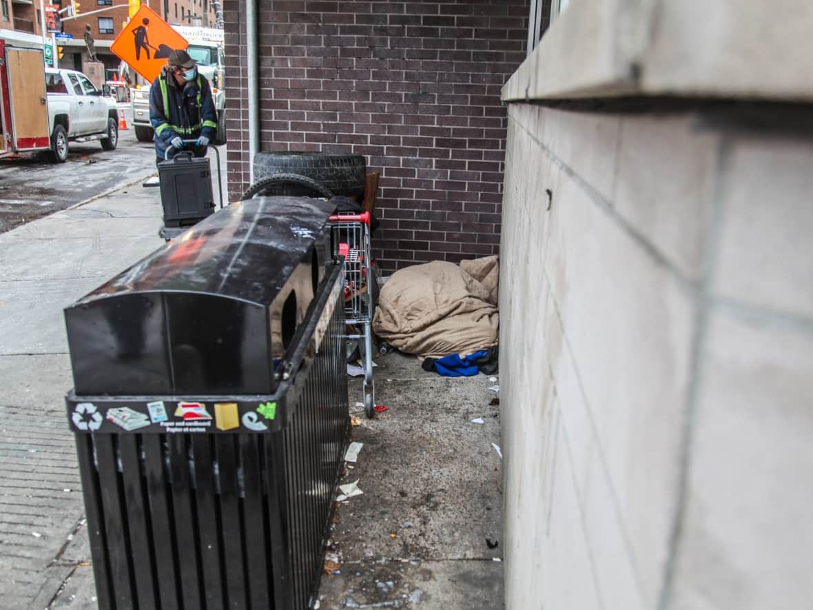 Outside the downtown headquarters of Youth Services Bureau of Ottawa, a man sleeps next to a cart loaded with his belongings. (Stu Mills/CBC - image credit)