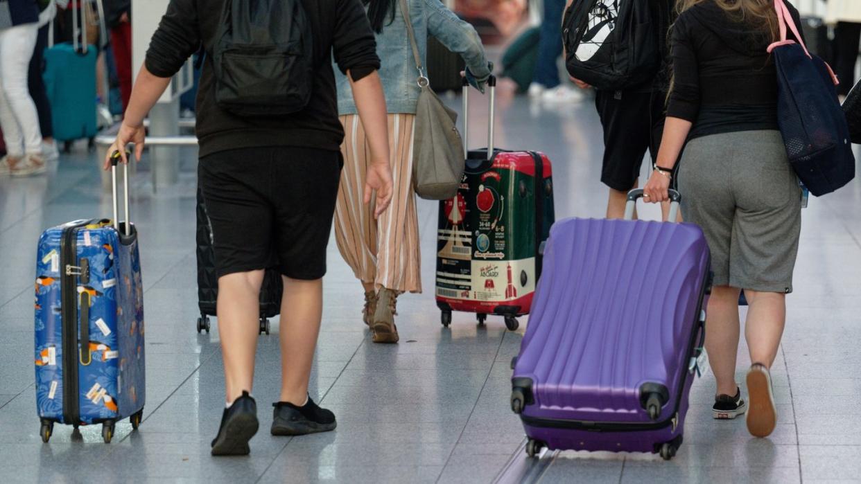 Reisende gehen im Flughafen Düsseldorf mit Koffern durch die Abflughalle.