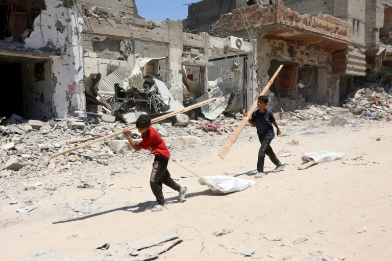 Dos muchachos palestinos cargan con sendos listones de madera para hacer fuego por una calle de edificios destruidos tras la retirada israelí después de una ofensiva de dos semanas contra el barrio de Shujaiya, el 11 de julio de 2024 en la ciudad de Gaza (Omar al Qattaa)
