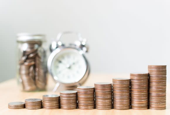 Step of coin stacks with a clock in the background.