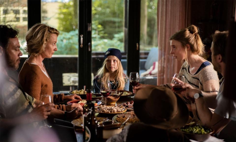 People gathered around a dinner table having a conversation. A young girl in a beanie sits at the center. Food and drinks are placed on the table. Names unknown