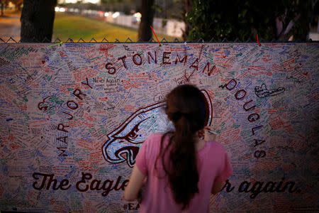 A girl writes a note on a banner placed on the fence of the Marjory Stoneman Douglas High School to commemorate the victims of the mass shooting, in Parkland, Florida, U.S., February 21, 2018. REUTERS/Carlos Garcia Rawlins