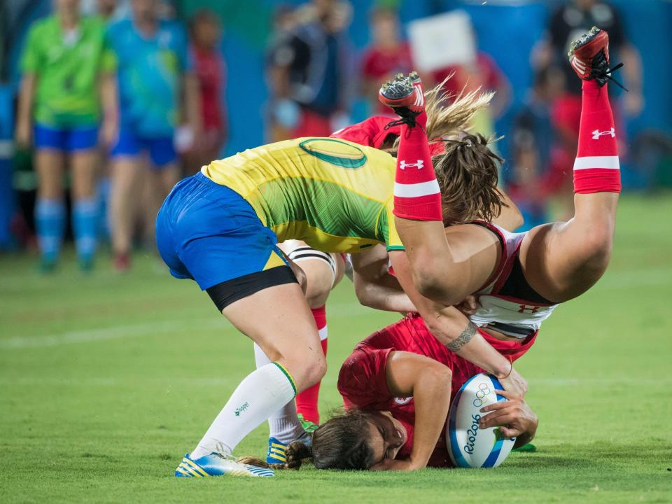 Women playing rugby flight for the ball - one is upside down with her head on the ground and arm around the ball