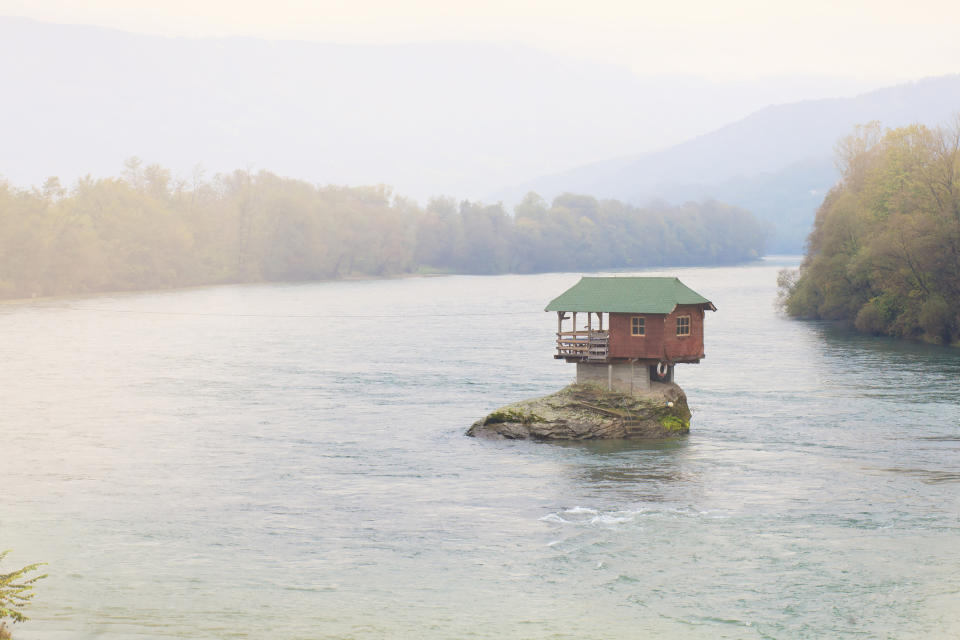 A lone house sitting on a rock surrounded by a river.