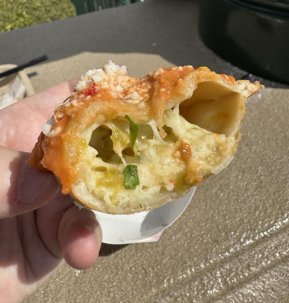 Hand holding a half-eaten cheese pizza slice with visible toppings. Used for a travel article about local cuisine