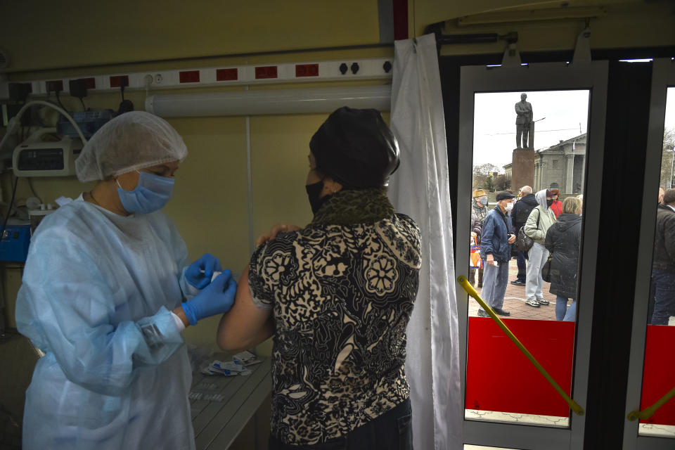 A Russian medical worker administers a shot of Russia's Sputnik V coronavirus vaccine for a woman as people wearing face masks to protect against coronavirus queue to get a shot of Russia's Sputnik V coronavirus vaccine in a mobile vaccination center with a statue of Vladimir Lenin in the background in Simferopol, Crimea, Tuesday, April 13, 2021. Russia has boasted about being the first country in the world to authorize a coronavirus vaccine and rushed to roll it out earlier than other countries, even as large-scale testing necessary to ensure its safety and effectiveness was still ongoing. (AP Photo/Alexander Polegenko)