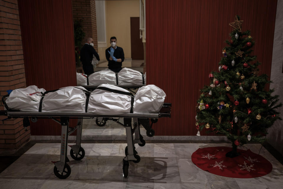 Mortuary workers take off their protective clothing at the entrance of a building decorated with a Christmas tree, after removing the body of person who is suspected of dying from COVID-19 in Barcelona, Spain, Dec. 23, 2020. The image was part of a series by Associated Press photographer Emilio Morenatti that won the 2021 Pulitzer Prize for feature photography. (AP Photo/Emilio Morenatti)