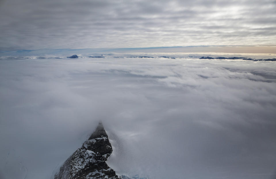 <p>A mountain (bottom left) peeks through clouds and ice as seen from NASA’s Operation IceBridge research aircraft, near the coast of the Antarctic Peninsula region on Oct. 31, 2017, above Antarctica. (Photo: Mario Tama/Getty Images) </p>